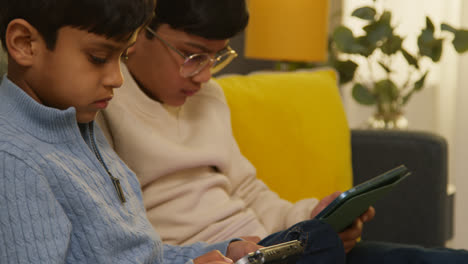 Two-Young-Boys-Sitting-On-Sofa-At-Home-Playing-Games-Or-Streaming-Onto-Digital-Tablets-12